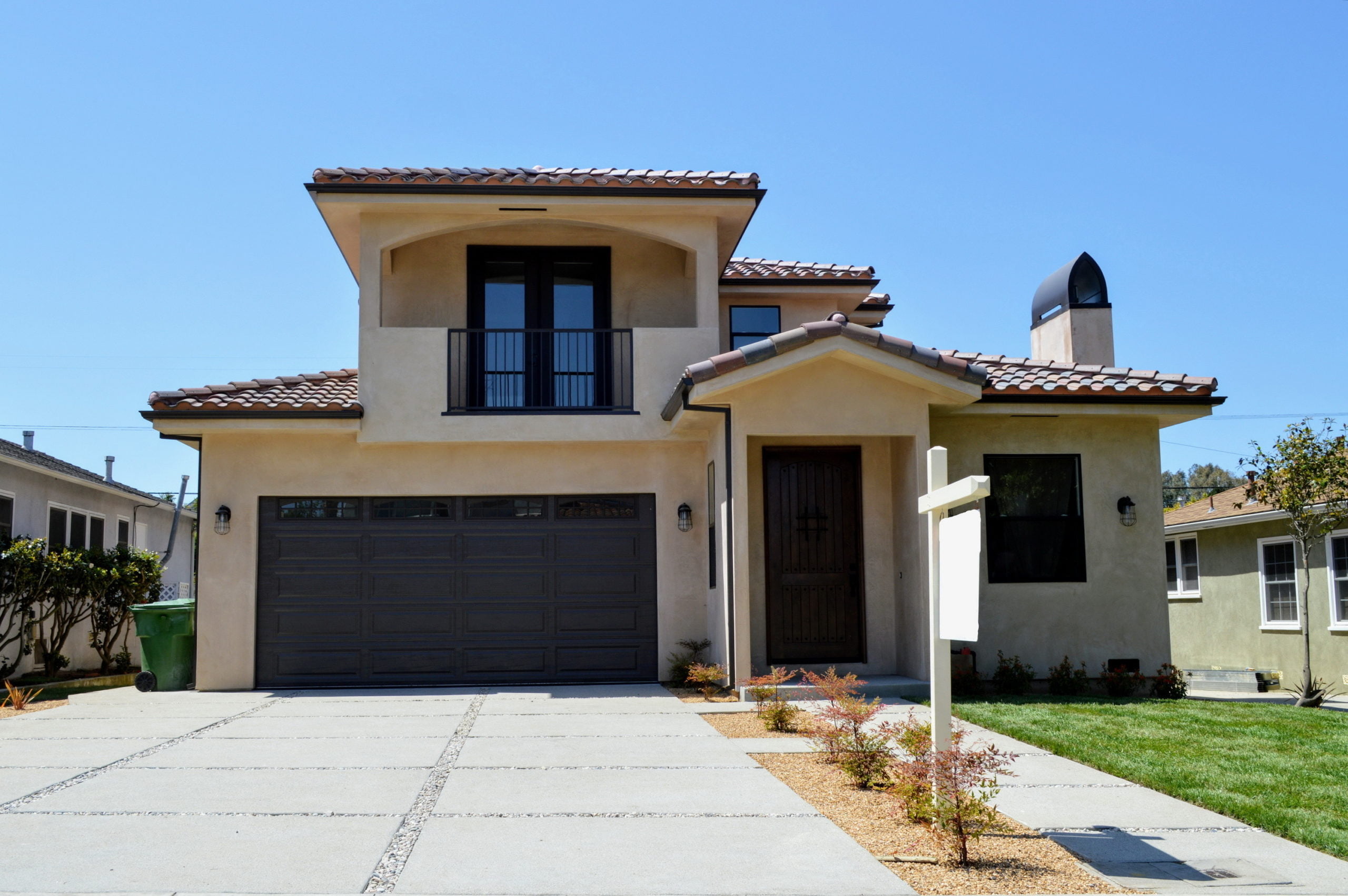 A beige house with a concrete driveway and a for sale sign, near where Core Alliance offers Northridge rental homes.